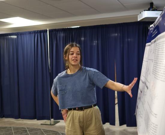 A student makes a presentation beside a poster at the 2024 Student Conference for 研究, 专业活动, 及创意艺术